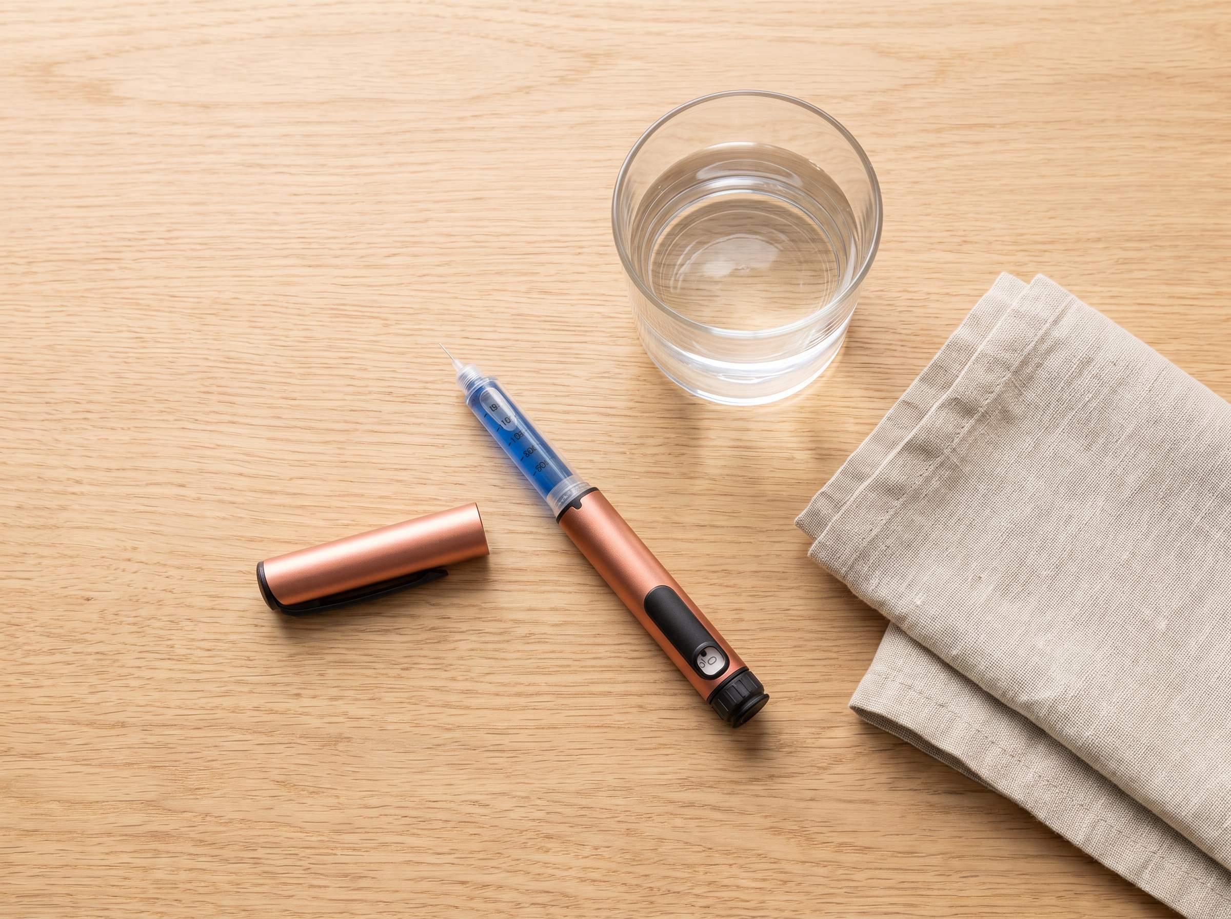A single copper research pen with its cap removed, laid on a wooden table beside a glass of water